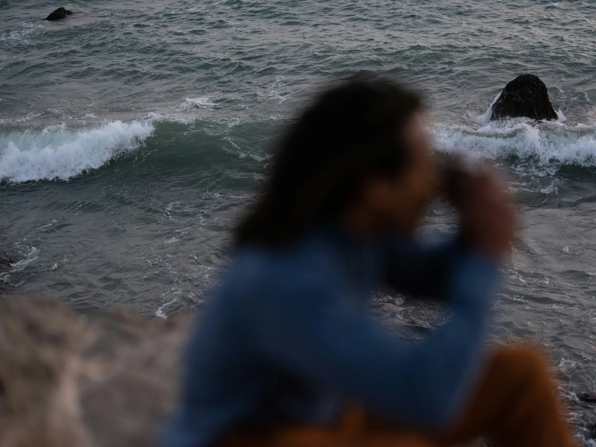 Een vrouw aan een rotsachtige kust met de zee op de achtergrond